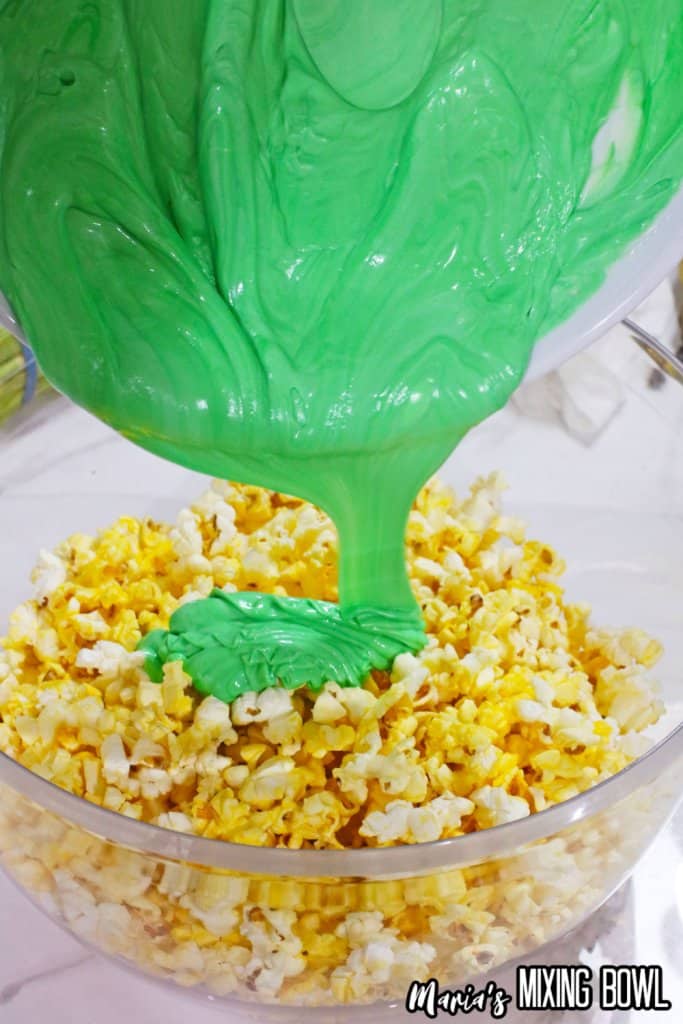 green almond bark being poured over a bowl of popped popcorn
