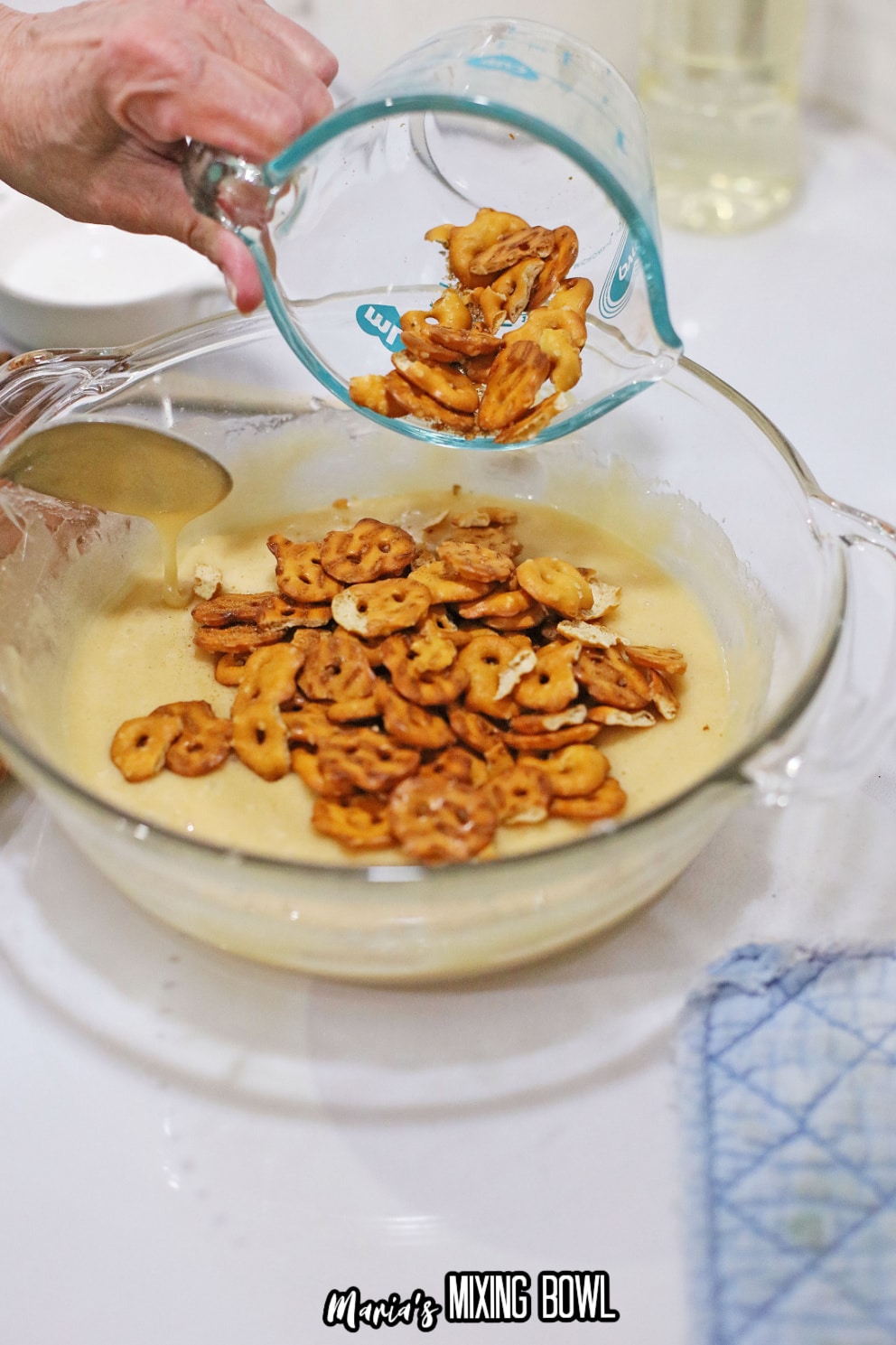 pretzels being added to the candy in a glass bowl