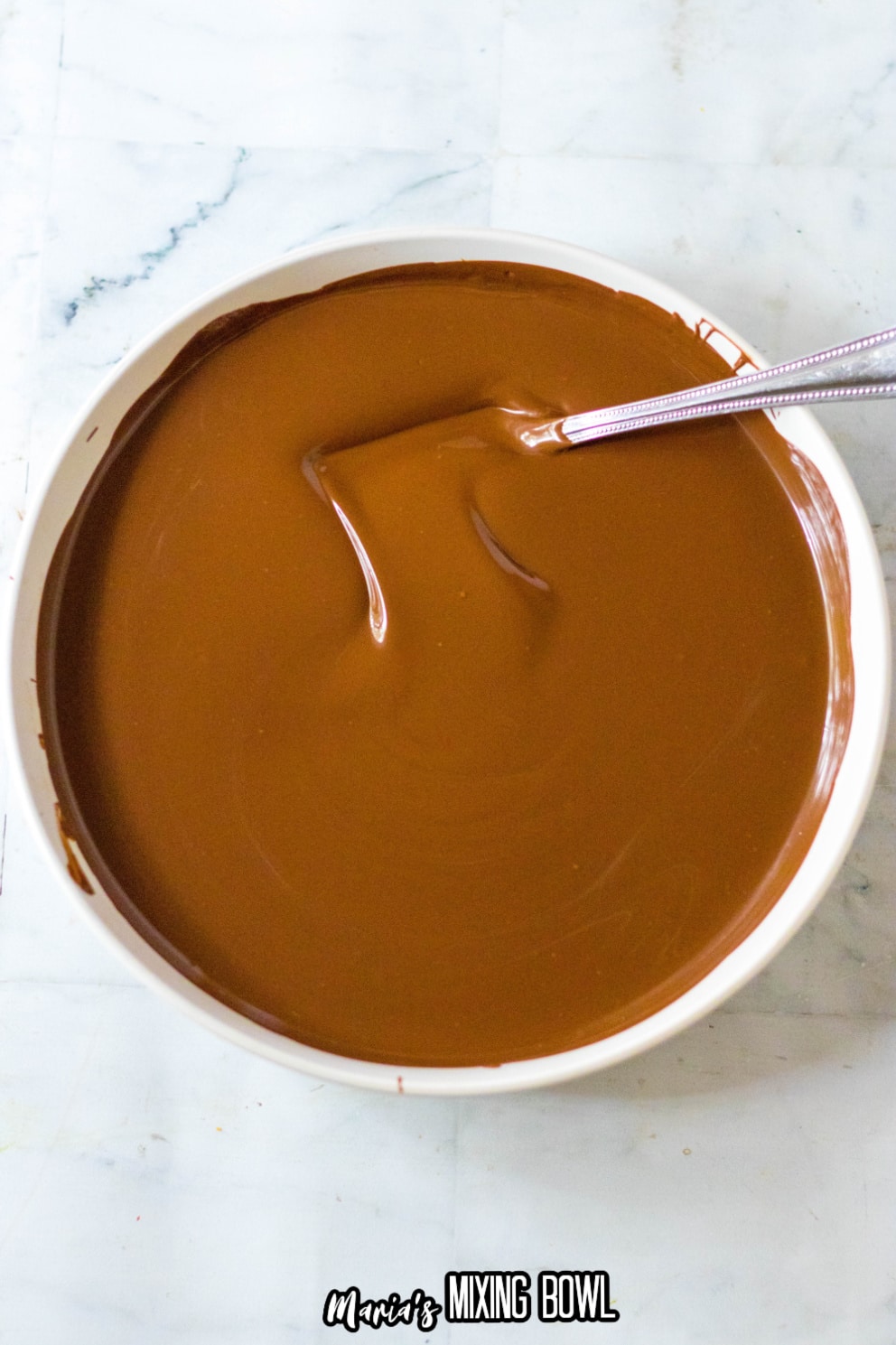 melted chocolate in a white bowl with a homemade candy being dipped in it