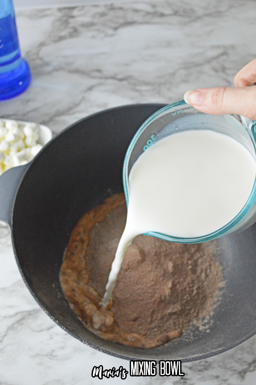 milk being added to a chocolate pudding mix in a dark mixing bowl