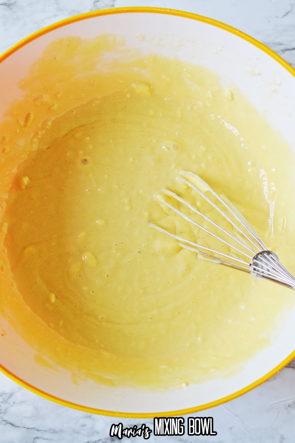 cake batter in a yellow and white mixing bowl with a whisk