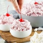 small white bowls filled with cherry fluff, with a women's fingers adding a cherry to the top with the name in text for pinterest
