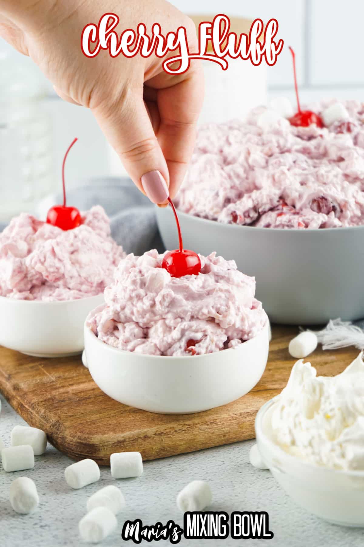small white bowls filled with cherry fluff, with a women's fingers adding a cherry to the top with the name in text for pinterest