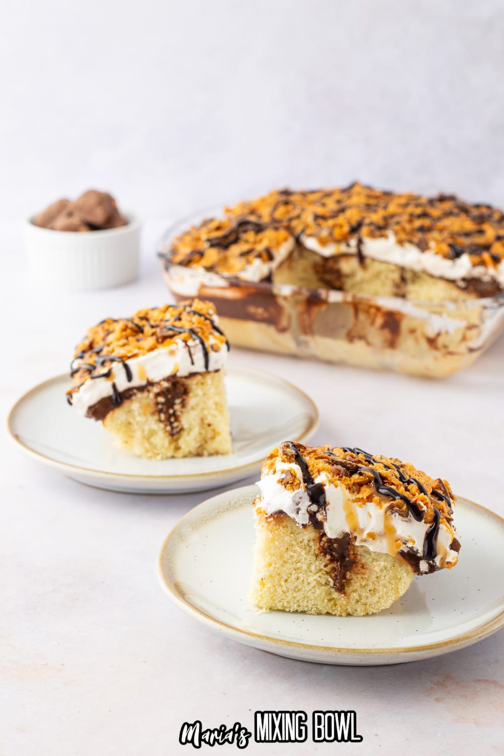 two slices of chocolate butterfinger poke cake with the whole cake in the background