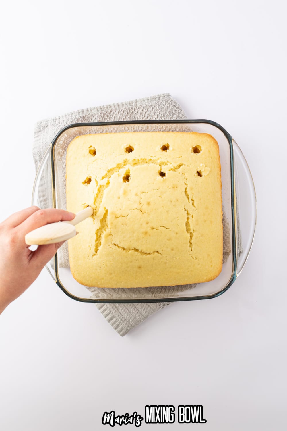 holes being poked into a baked cake in a glass baking dish