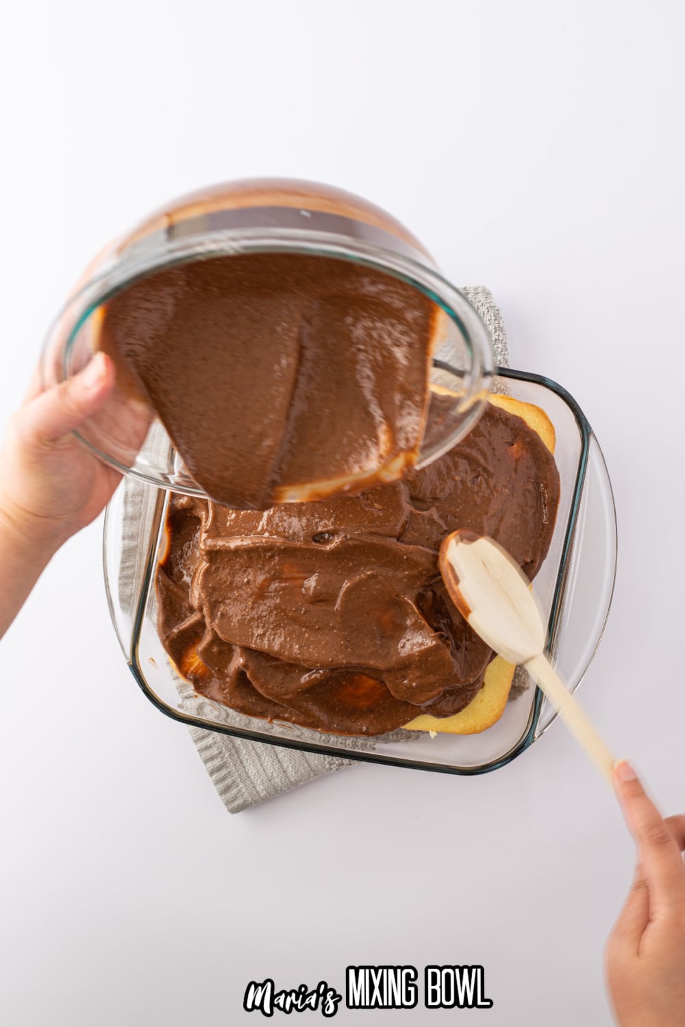 chocolate pudding being spread on top of a cake in a glass baking dish