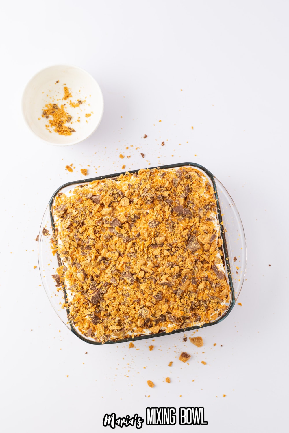 crushed butterfingers being spread on top of a cake in a glass baking dish