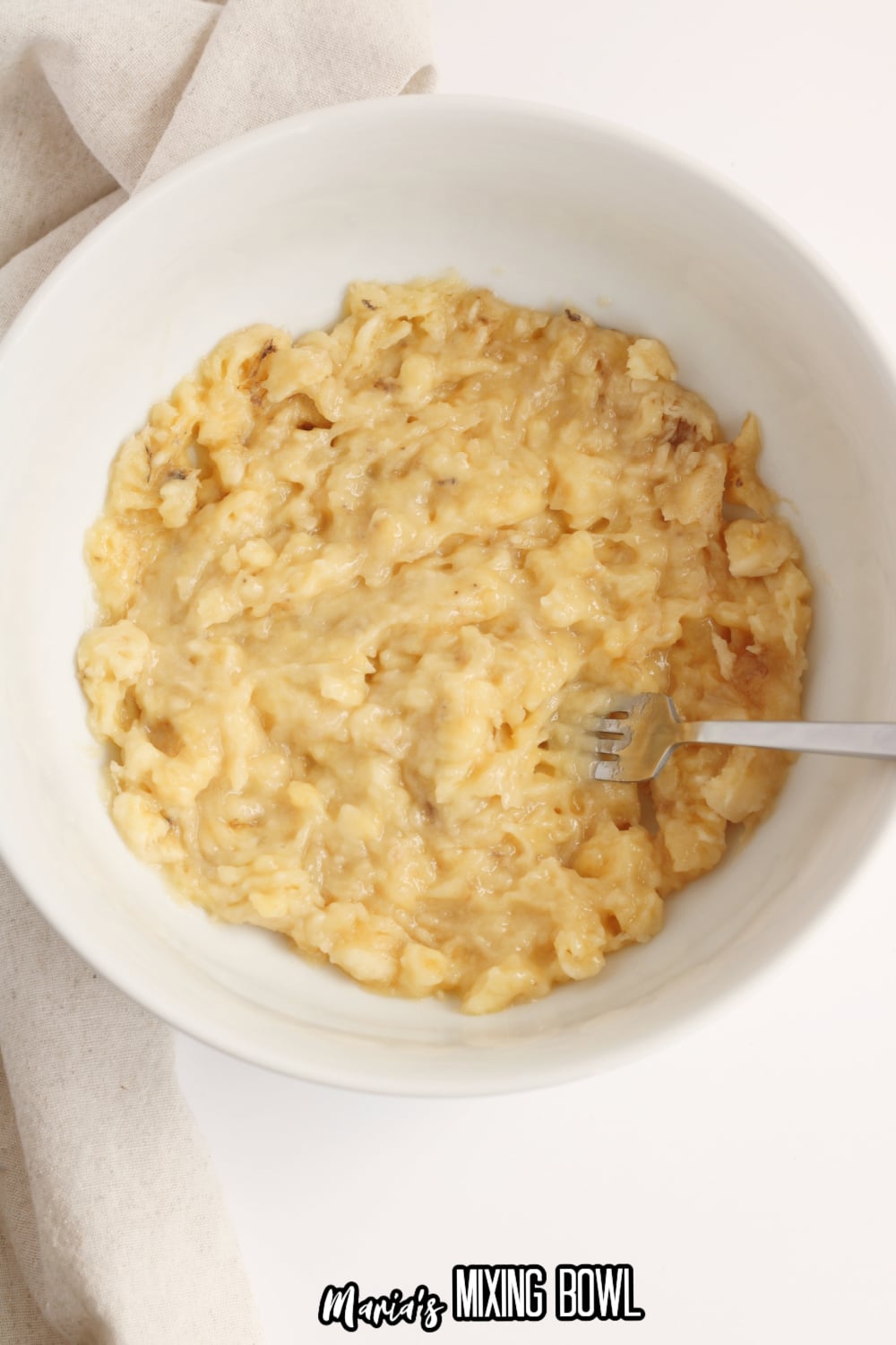 bananas being mashed in a white mixing bowl