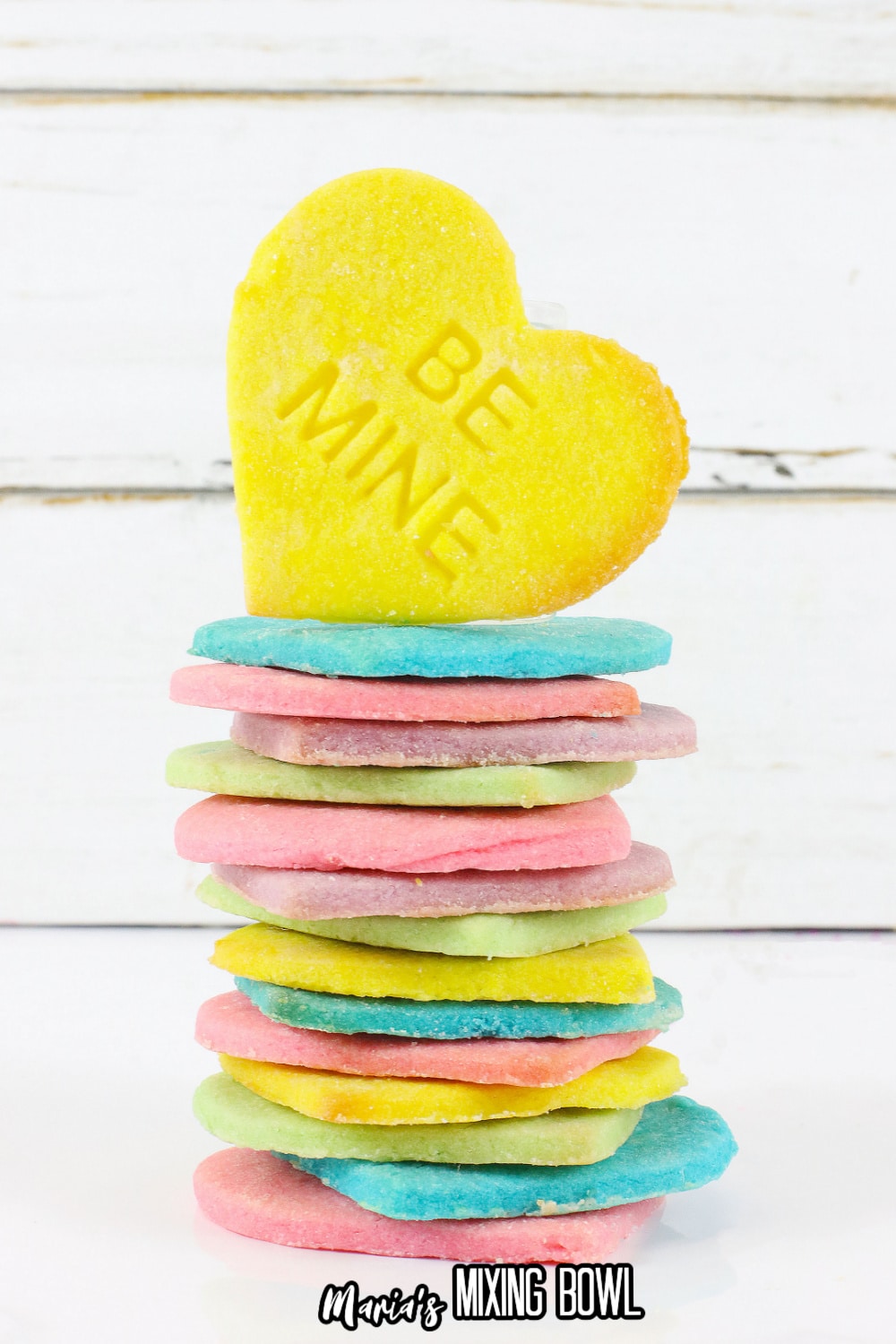 conversation heart cookies stacked on a white background with a yellow cookie on top