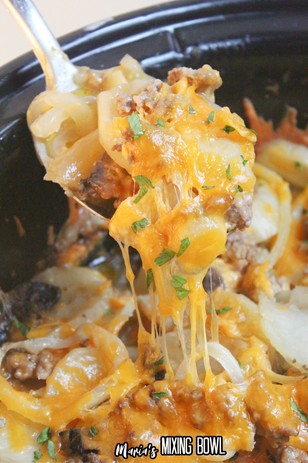 beef and potato au gratin on a spoon held above a crockpot full of it