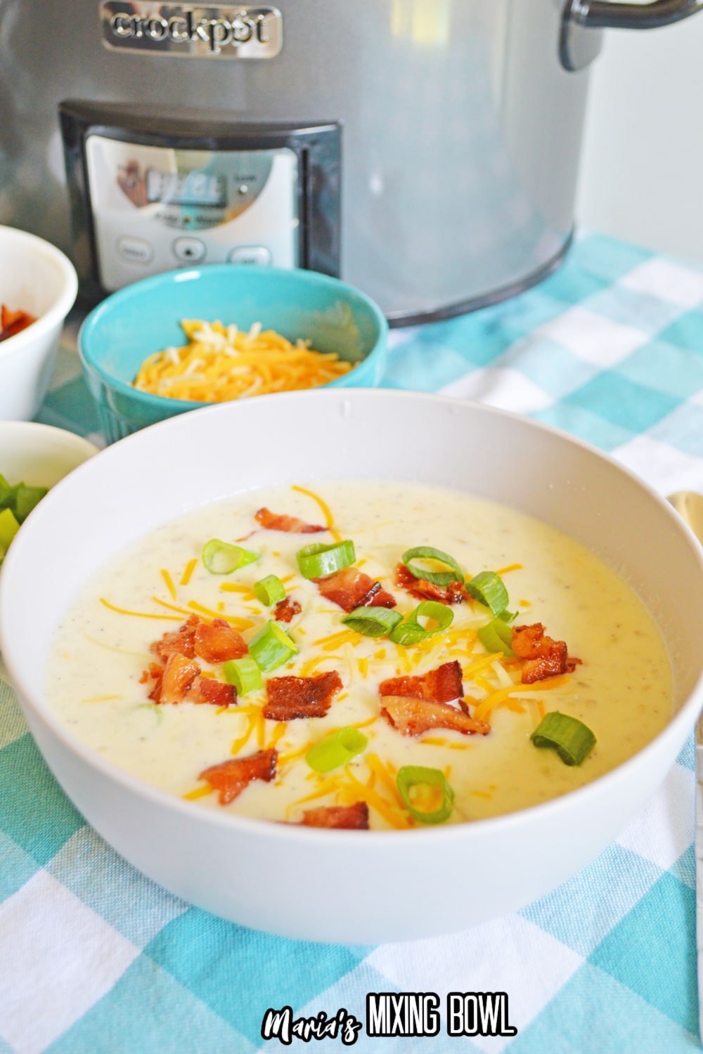 white bowl filled with crockpot loaded potato soup with bacon, green onions, and shredded cheese
