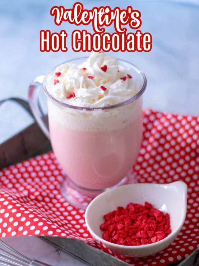glass mug full of pink hot chocolate topped with whipped cream and red heart sprinkles with the name in text for pinterest