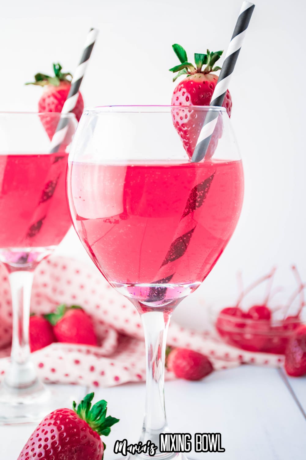 wine glass full of cupids cocktail with a strawberry on the rim with a black and white straw.