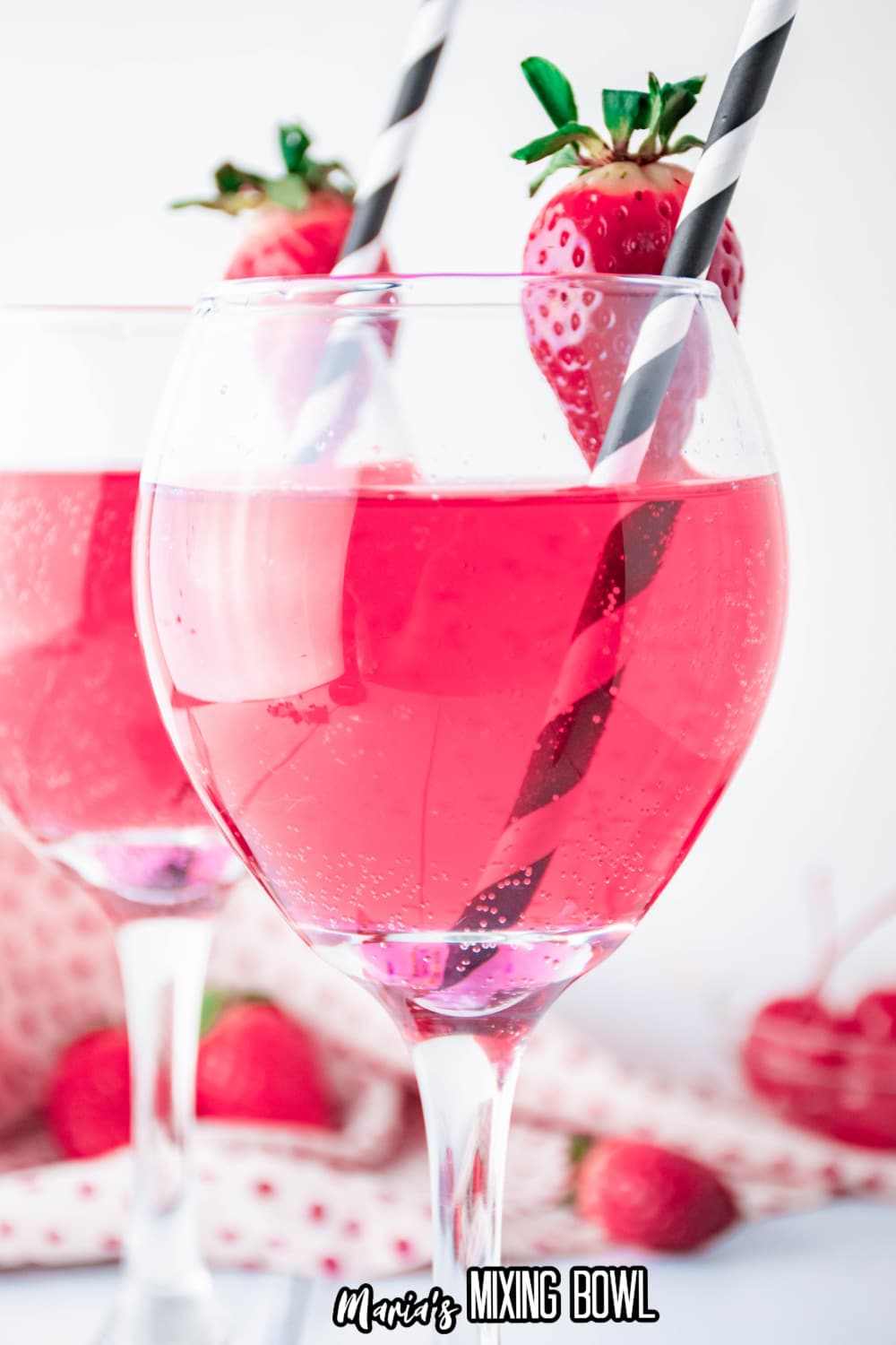 wine glass full of cupids cocktail with a strawberry on the rim with a black and white straw.