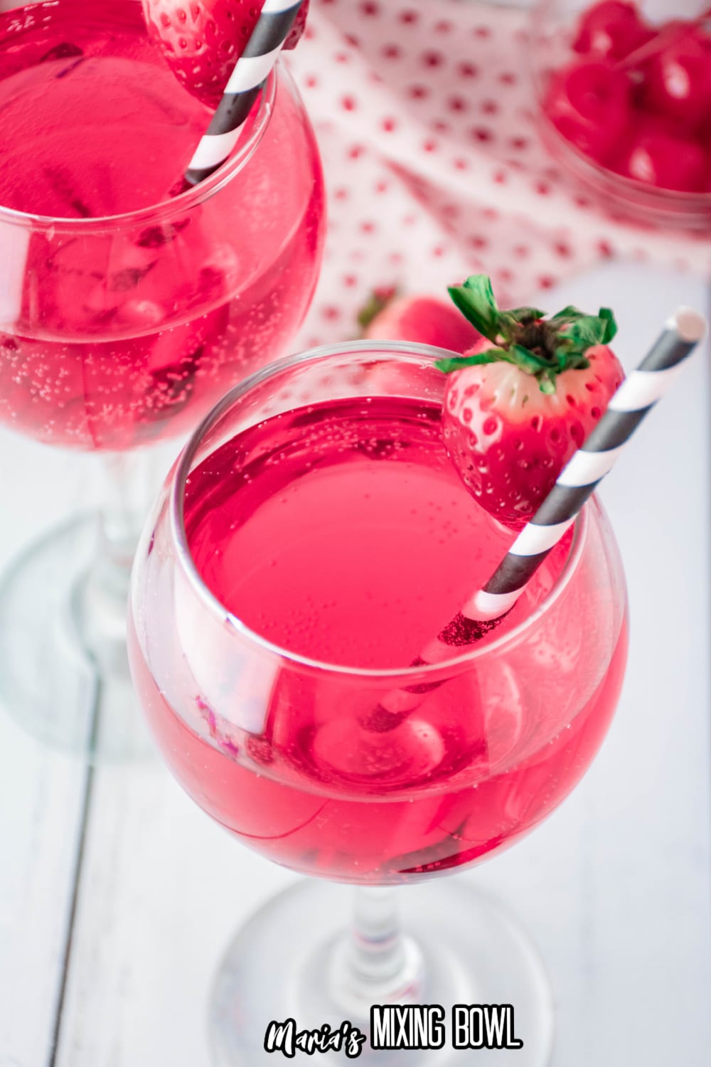 birds eye view of a wine glass full of cupids cocktail with a strawberry on the rim with a black and white straw.