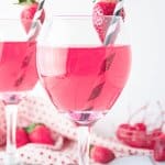 wine glass full of cupids cocktail with a strawberry on the rim with a black and white straw. with the name in text for pinterest