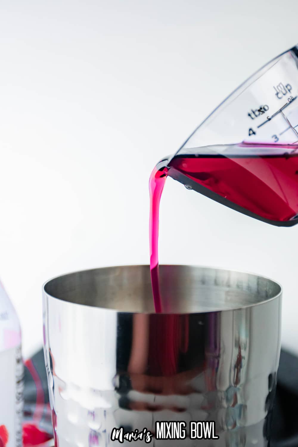 Strawberry rum being poured into a stainless steel cocktail shaker