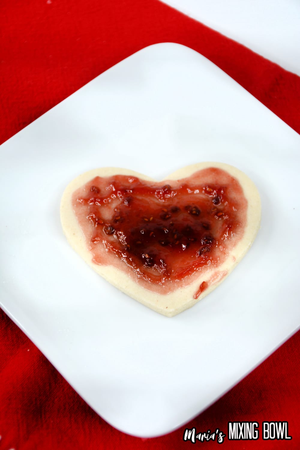 jam being spread into a sugar cookie on a white plate