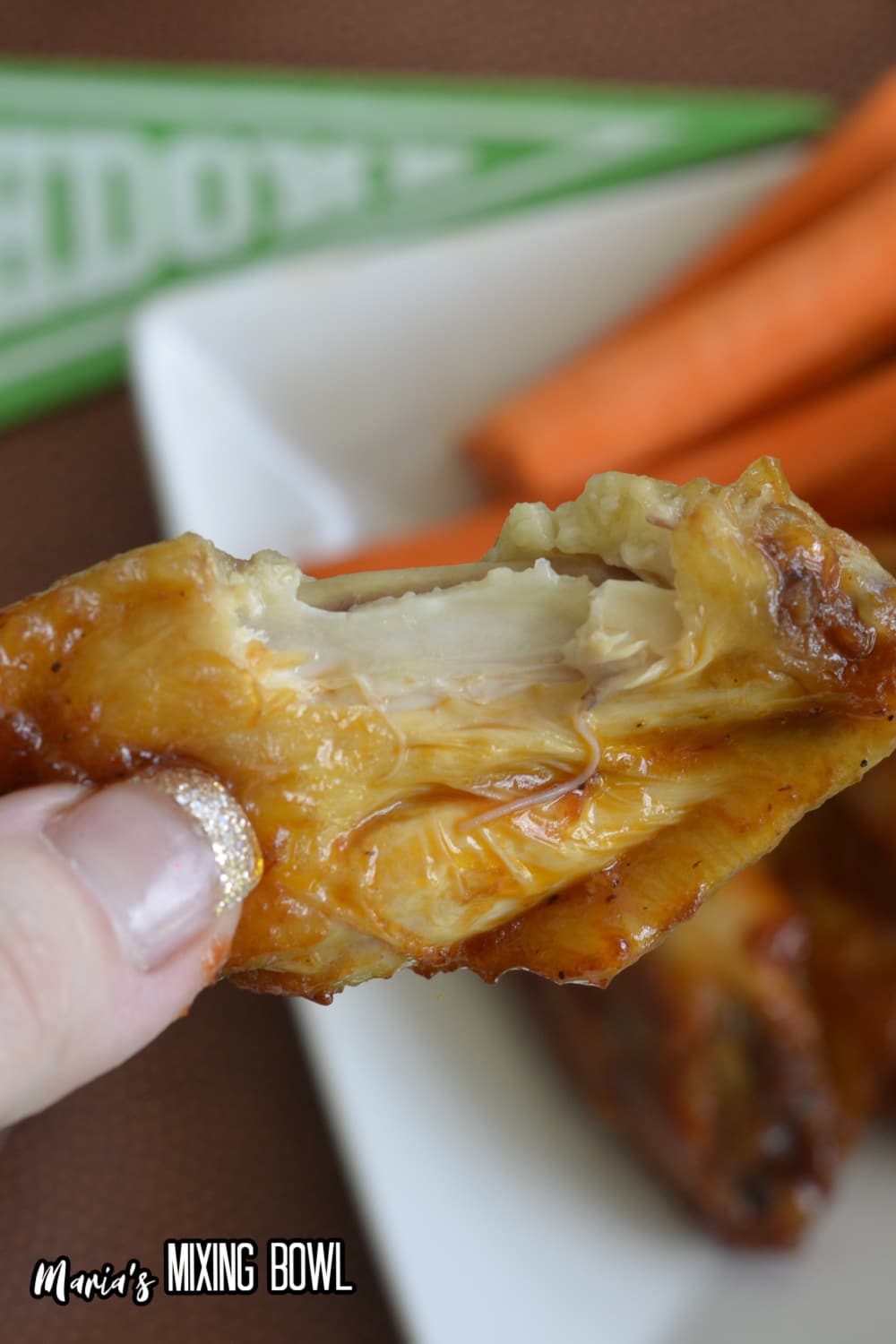 chicken wing held in a womans fingers with a bite missing