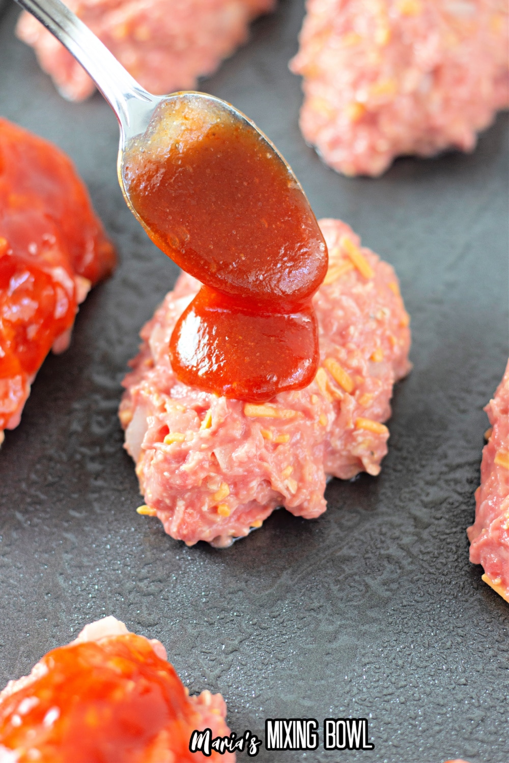sauce being added on top of a mini meatloaf on a baking sheet
