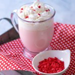 glass mug full of pink hot chocolate topped with whipped cream and red heart sprinkles