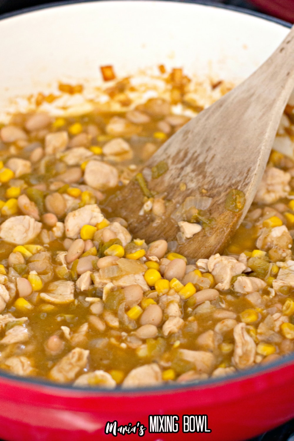 ingredients being stirred in a red dutch oven with a wooden spoon