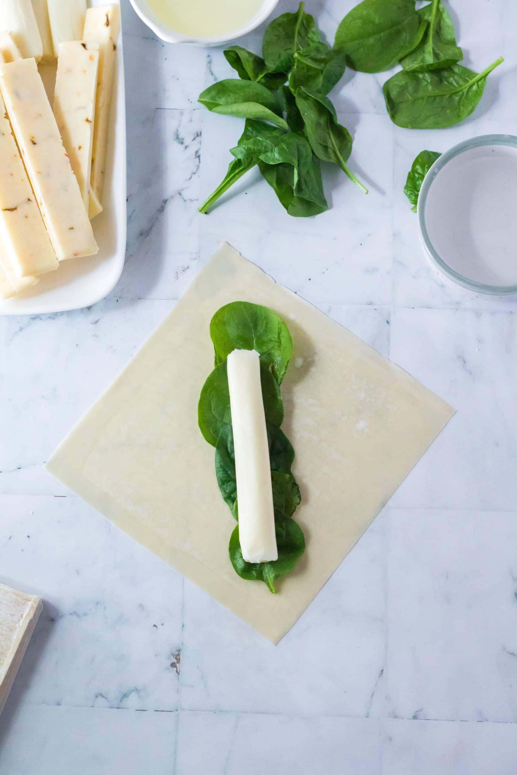 cheese stick being rolled into a wonton wrapper
