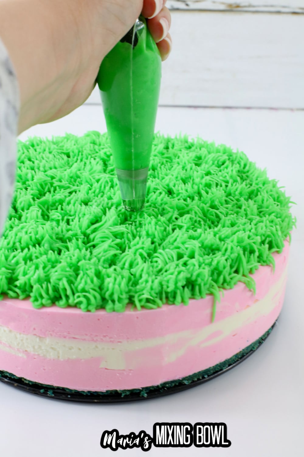 green frosting being piped on top of a cheesecake