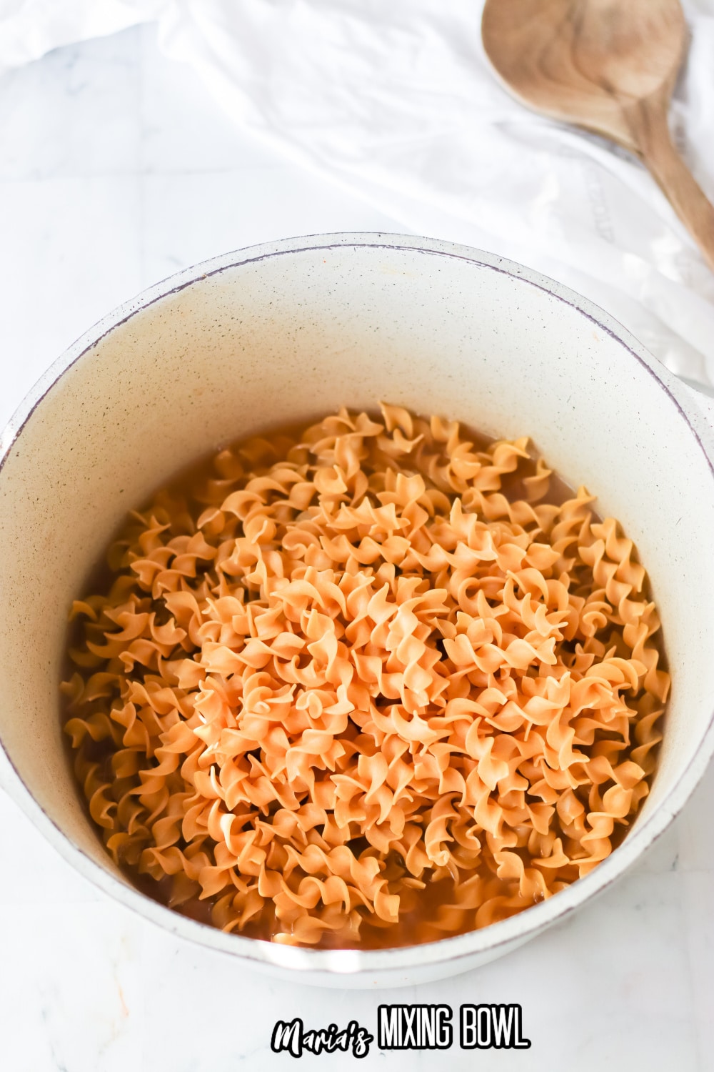 raw egg noodles and chicken broth in a white pot
