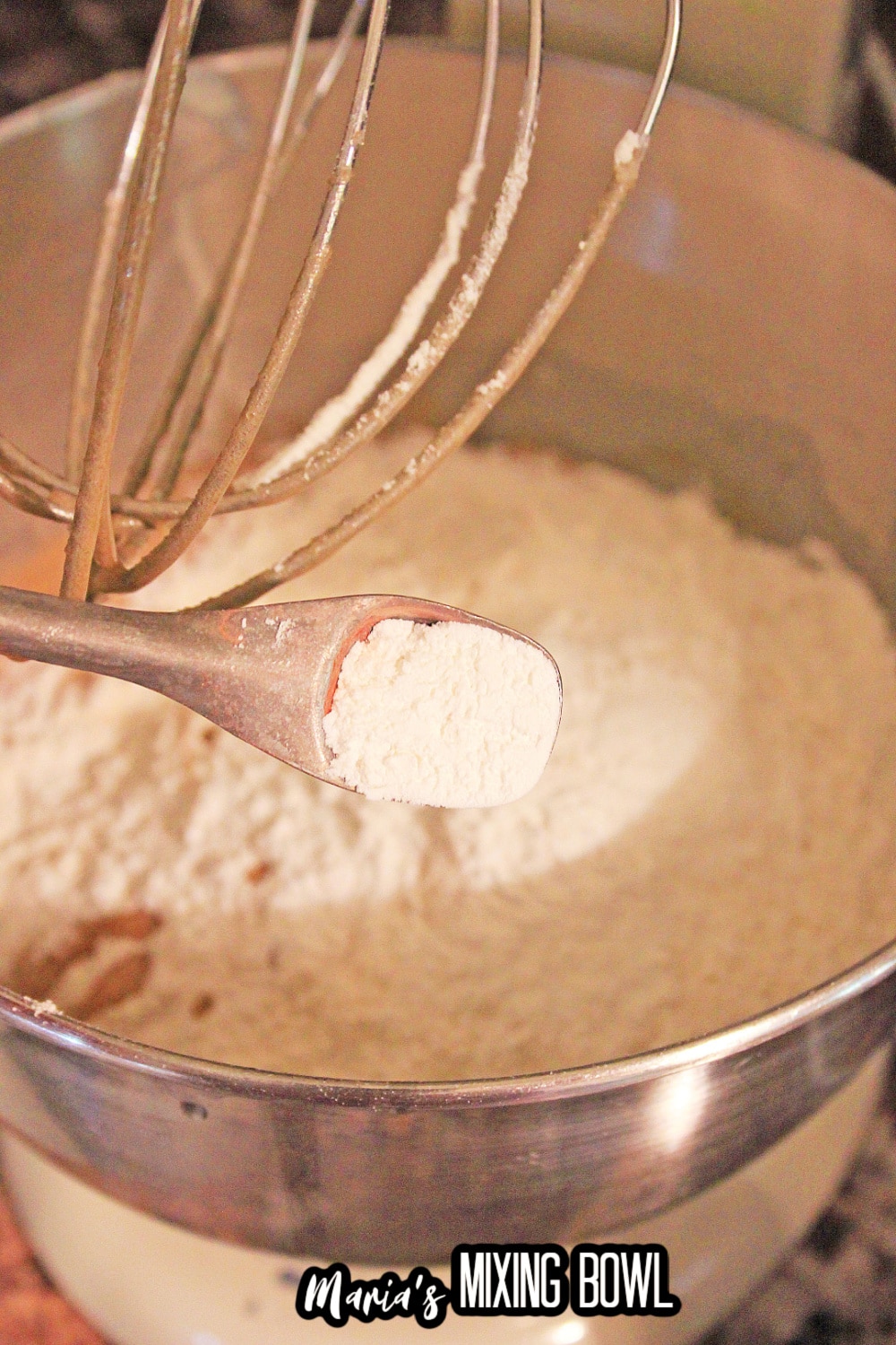 dry ingredients being added to a stand mixer with a whisk attachment