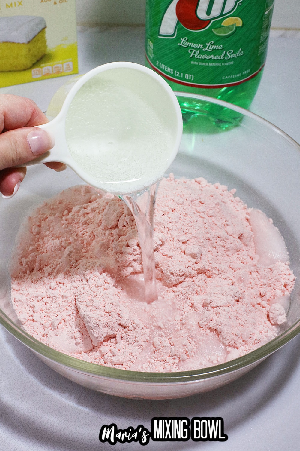 powdered mix in a glass mixing bowl and 7up being poured into the cake