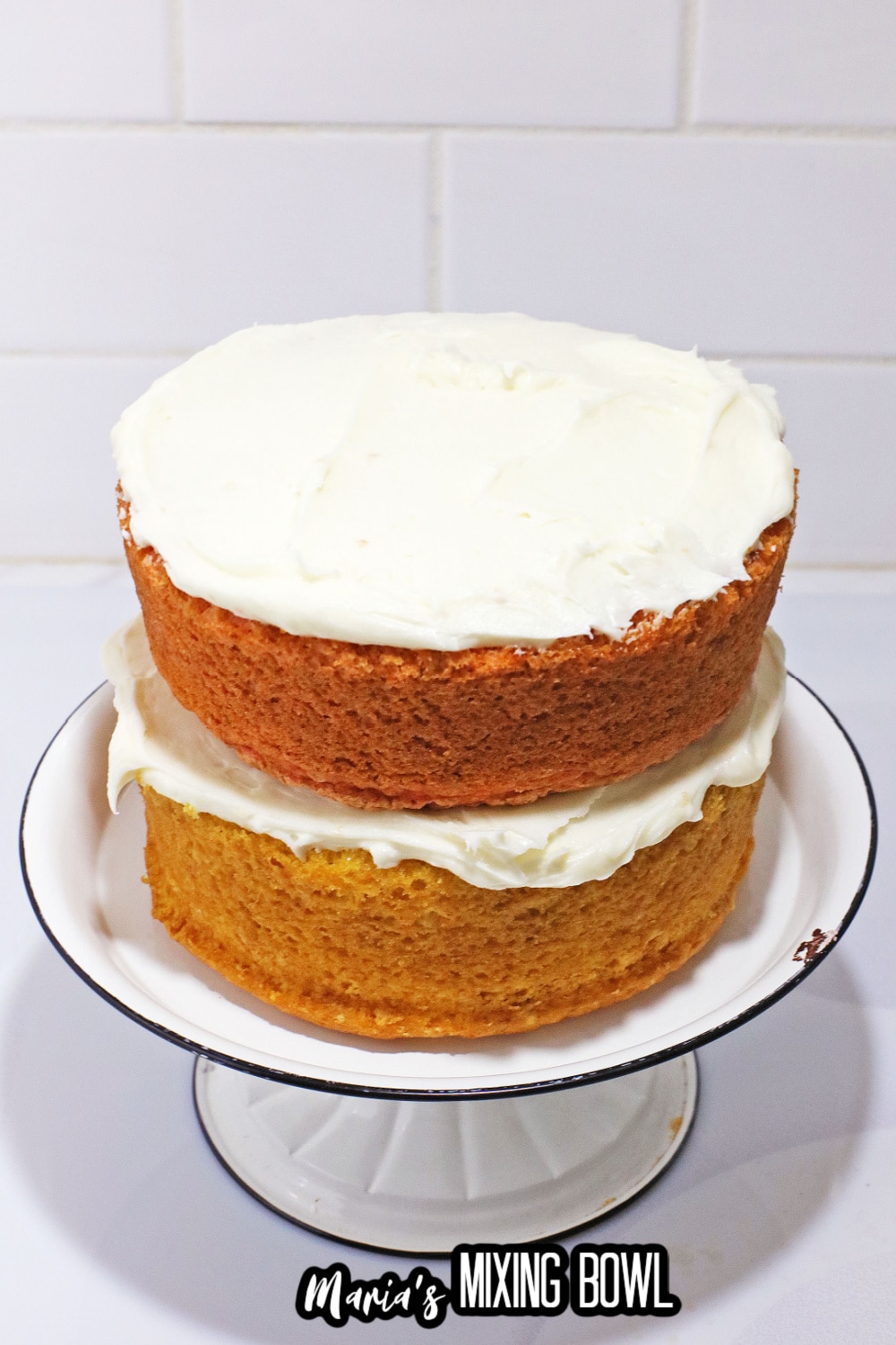 cake layers on a white cake stand being frosted with vanilla frosting