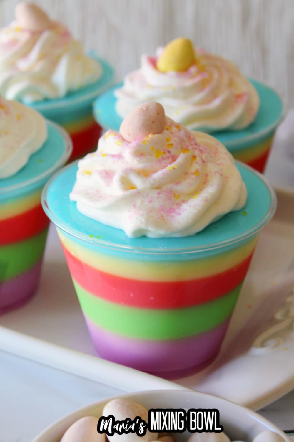 small plastic cups filled with colorful easter layered jello and topped with whipped cream