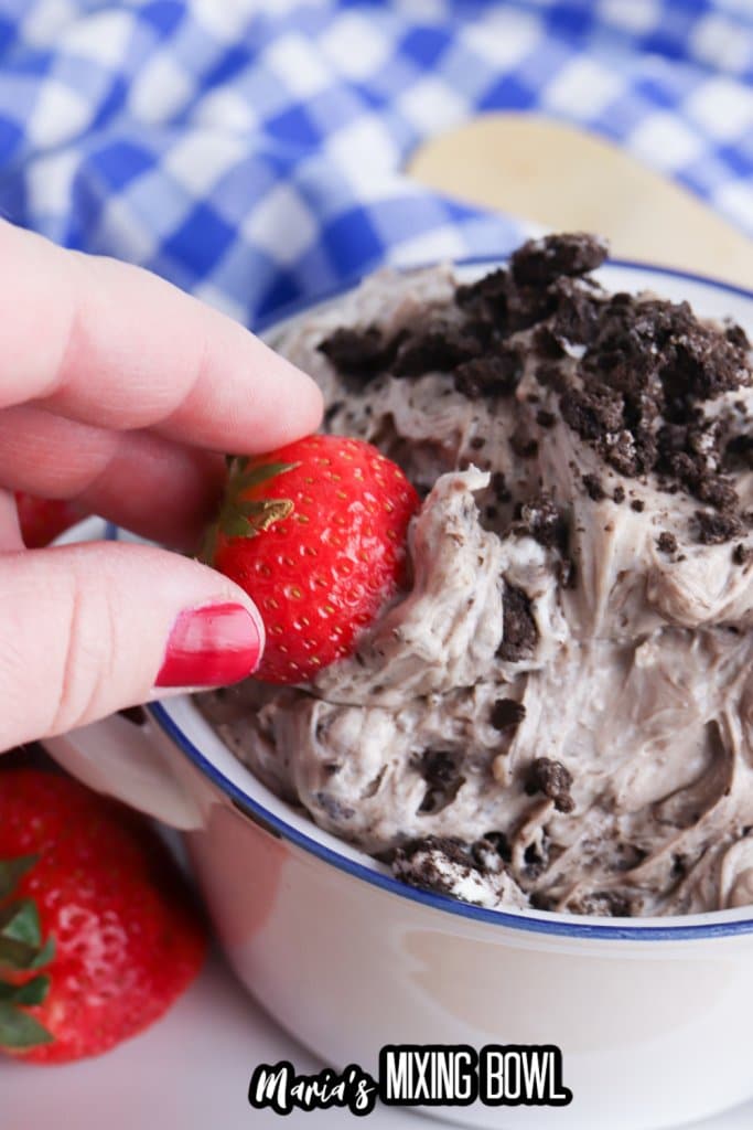strawberry being dipped oreo cheesecake dip in a white bowl