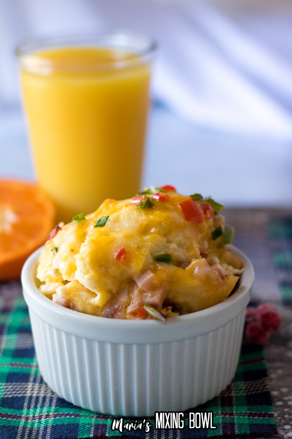 scoop of overnight egg casserole in a ceramic ramekin with a glass of orange juice in the background