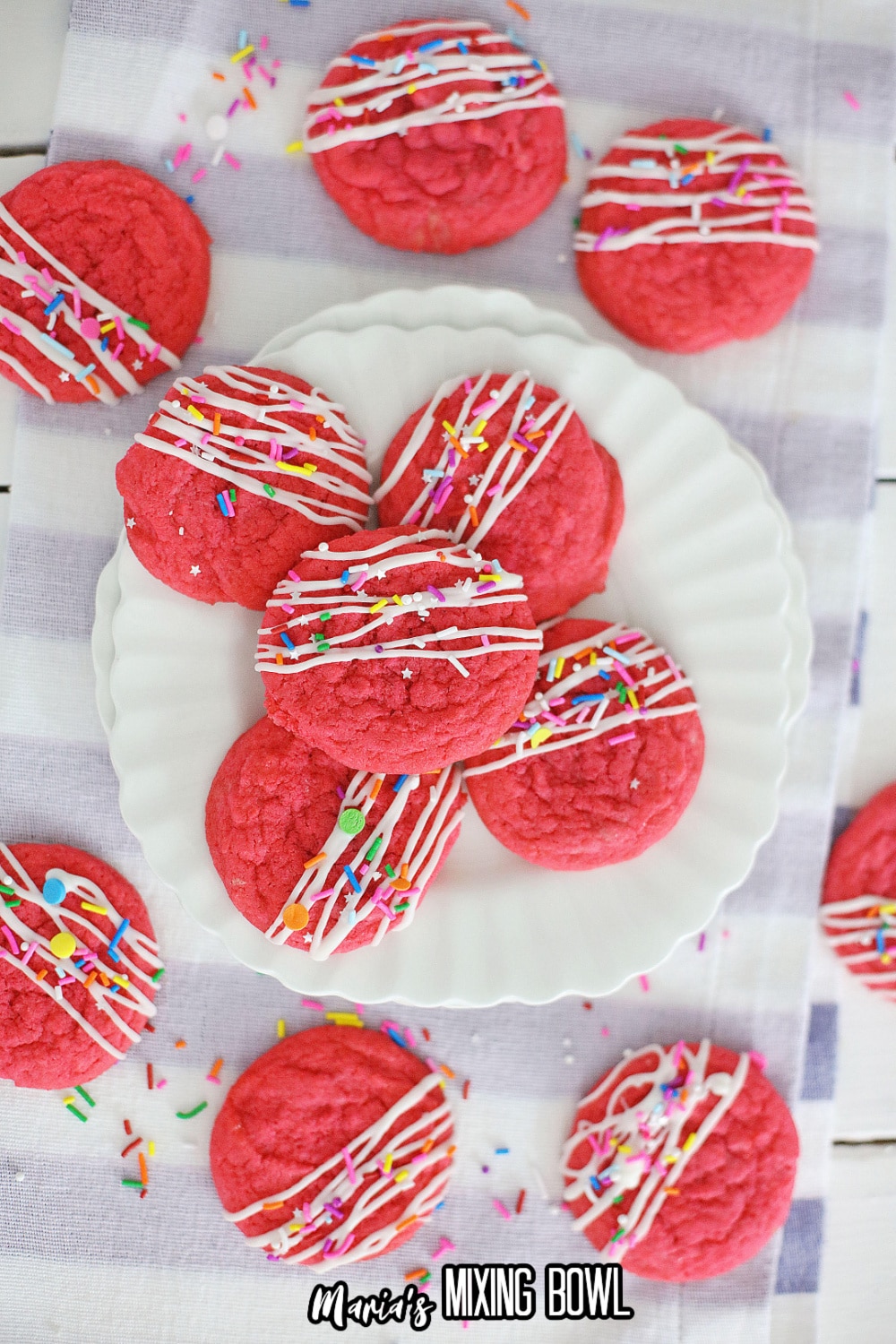 five pink velvet cookies on a white scalloped plate with extra cookies above and below the plate