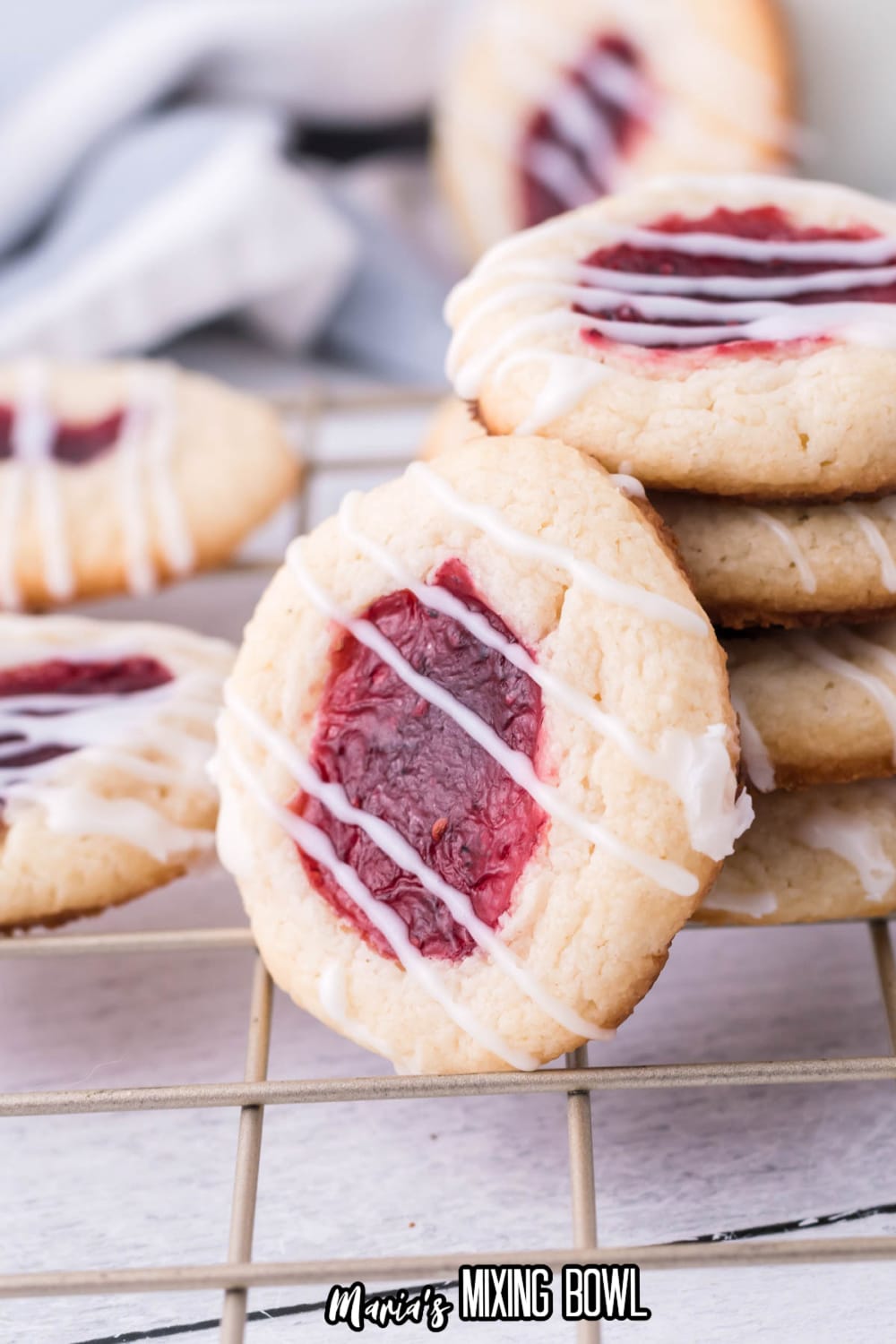 stack of raspberry cheesecake thumbprint cookies with one cookie on it's side leaning against the others