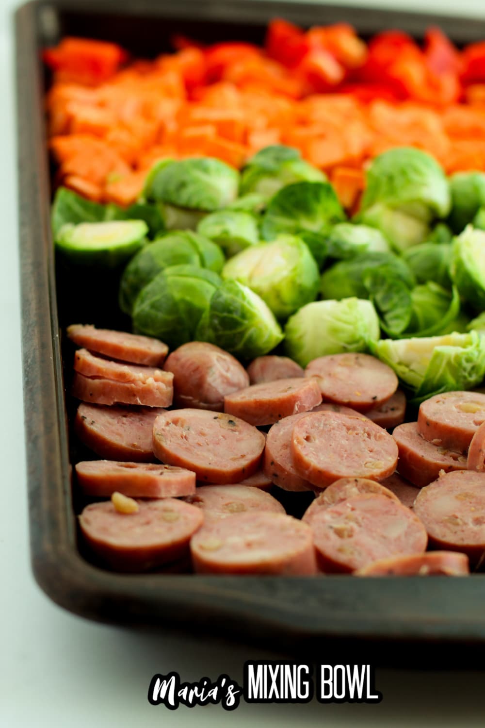 uncooked sausage, brussel sprouts, sweet potatoes and peppers on a sheet pan