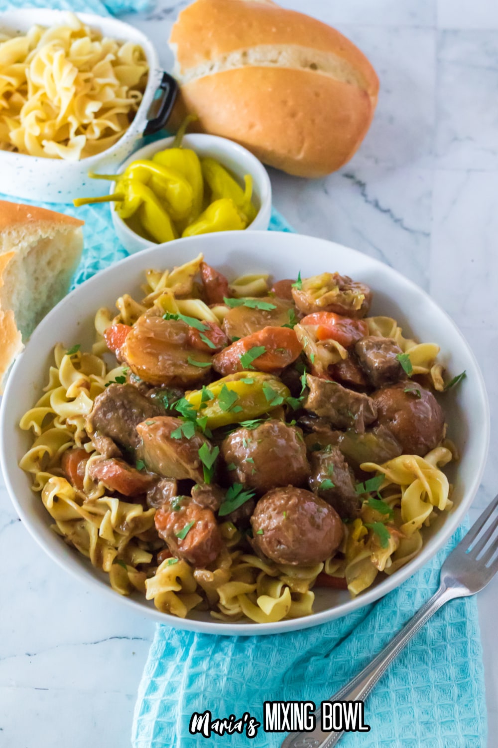 white bowl filled with egg noodles topped with slow cooker Mississippi beef stew.