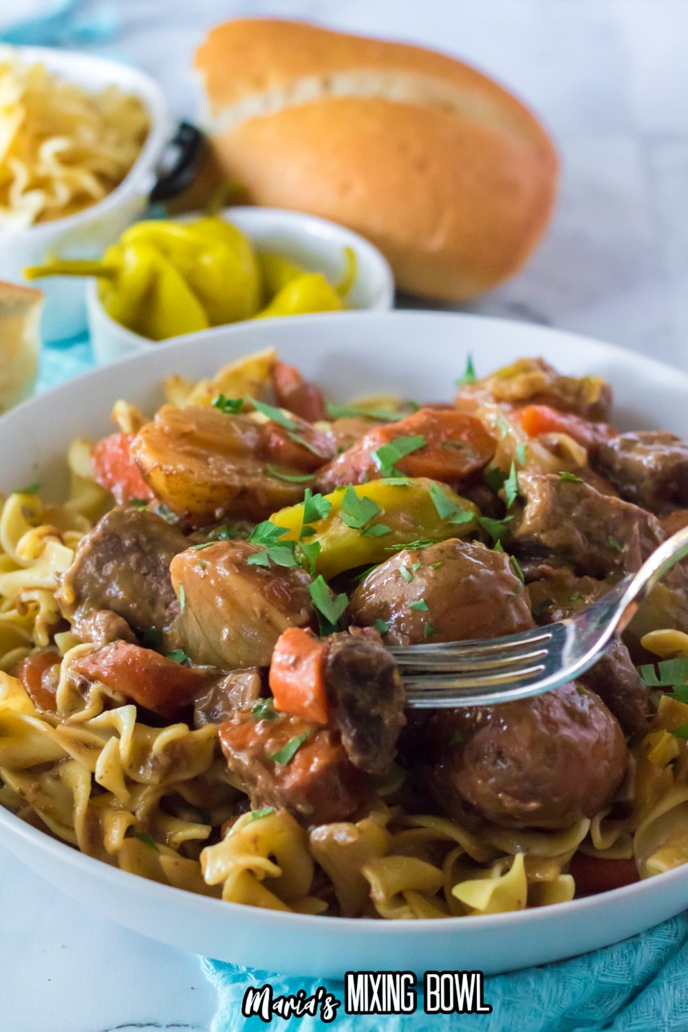 white bowl filled with egg noodles topped with slow cooker Mississippi beef stew.