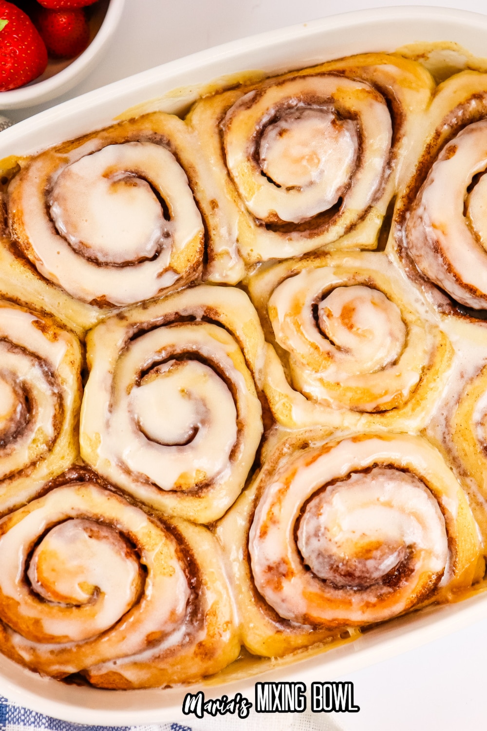 frosted cinnamon rolls in a white ceramic baking dish