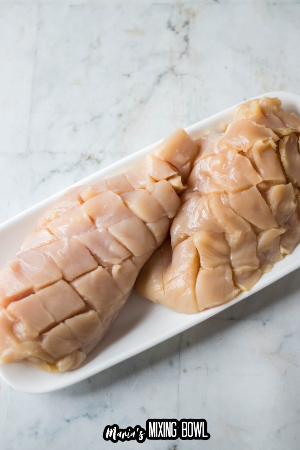 raw chicken breasts scored on a white plate