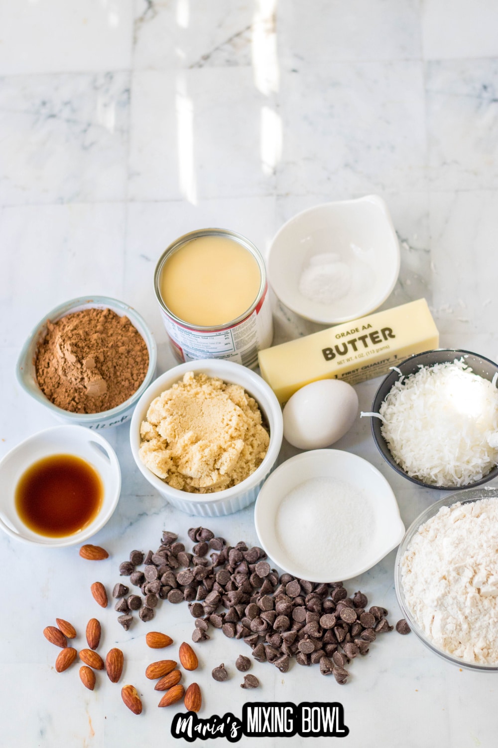 butter, sugar, flour, coconut, egg, chocolate chip, vanilla, cocoa powder, and sweetened condensed milk on a marble counter
