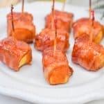 pieces of bacon wrapped pineapple on a white plate
