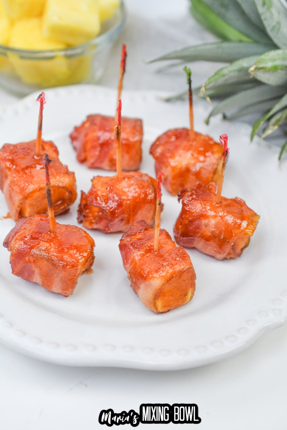 pieces of bacon wrapped pineapple on a white plate