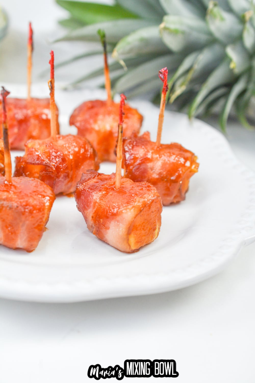 pieces of bacon wrapped pineapple on a white plate
