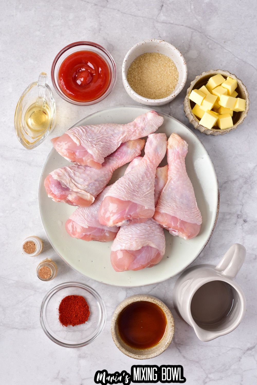chicken drumsticks, ketchup, butter, and seasonings on a marble background