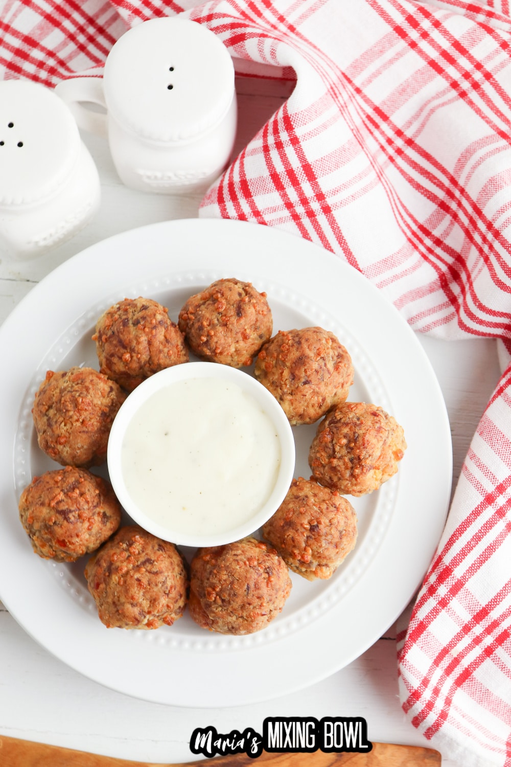 birds eye image of bisquick sausage balls on a white plate with a small bowl of gravy in the center