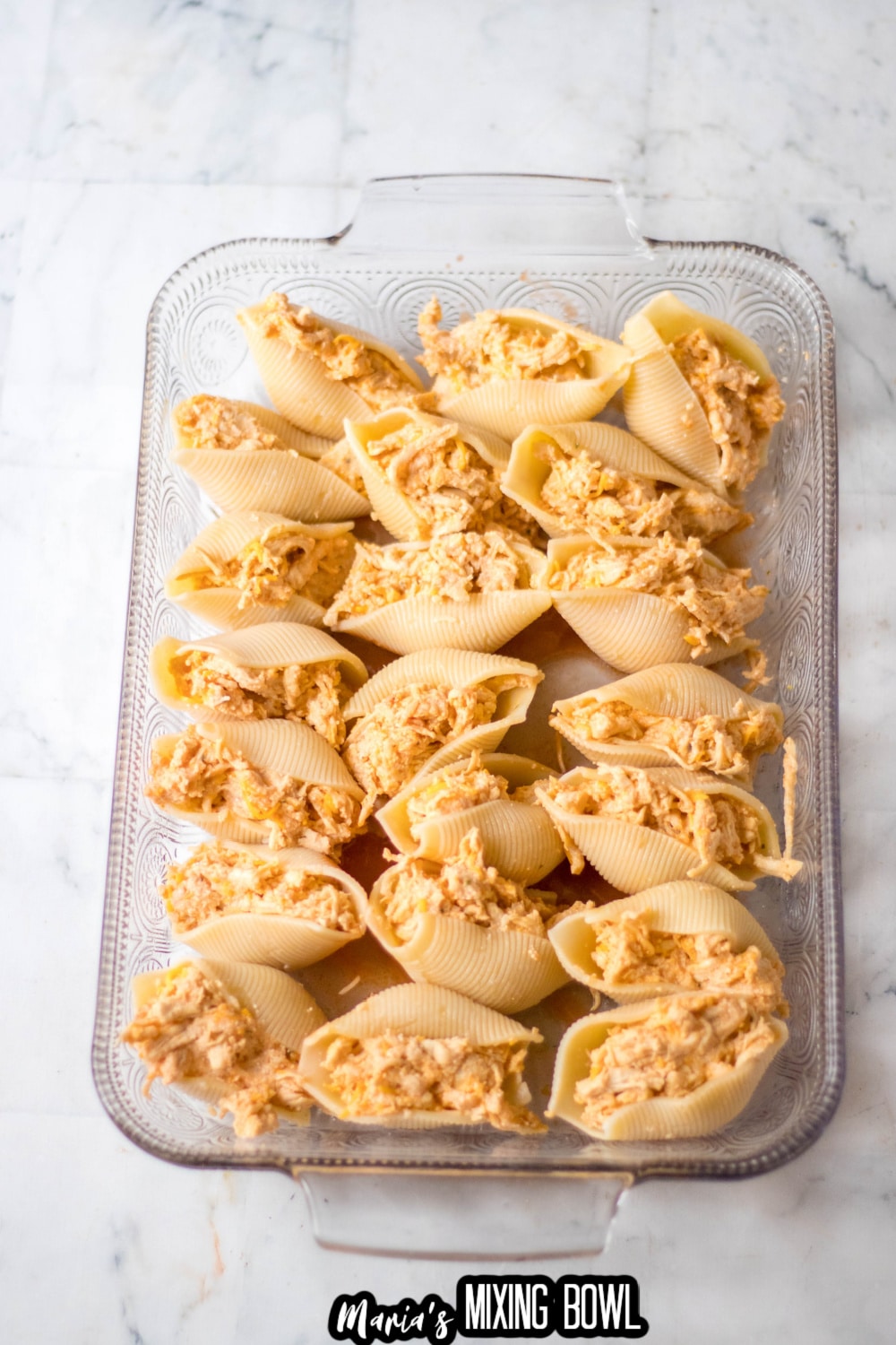 shells being stuffed with chicken and added to a baking sheet