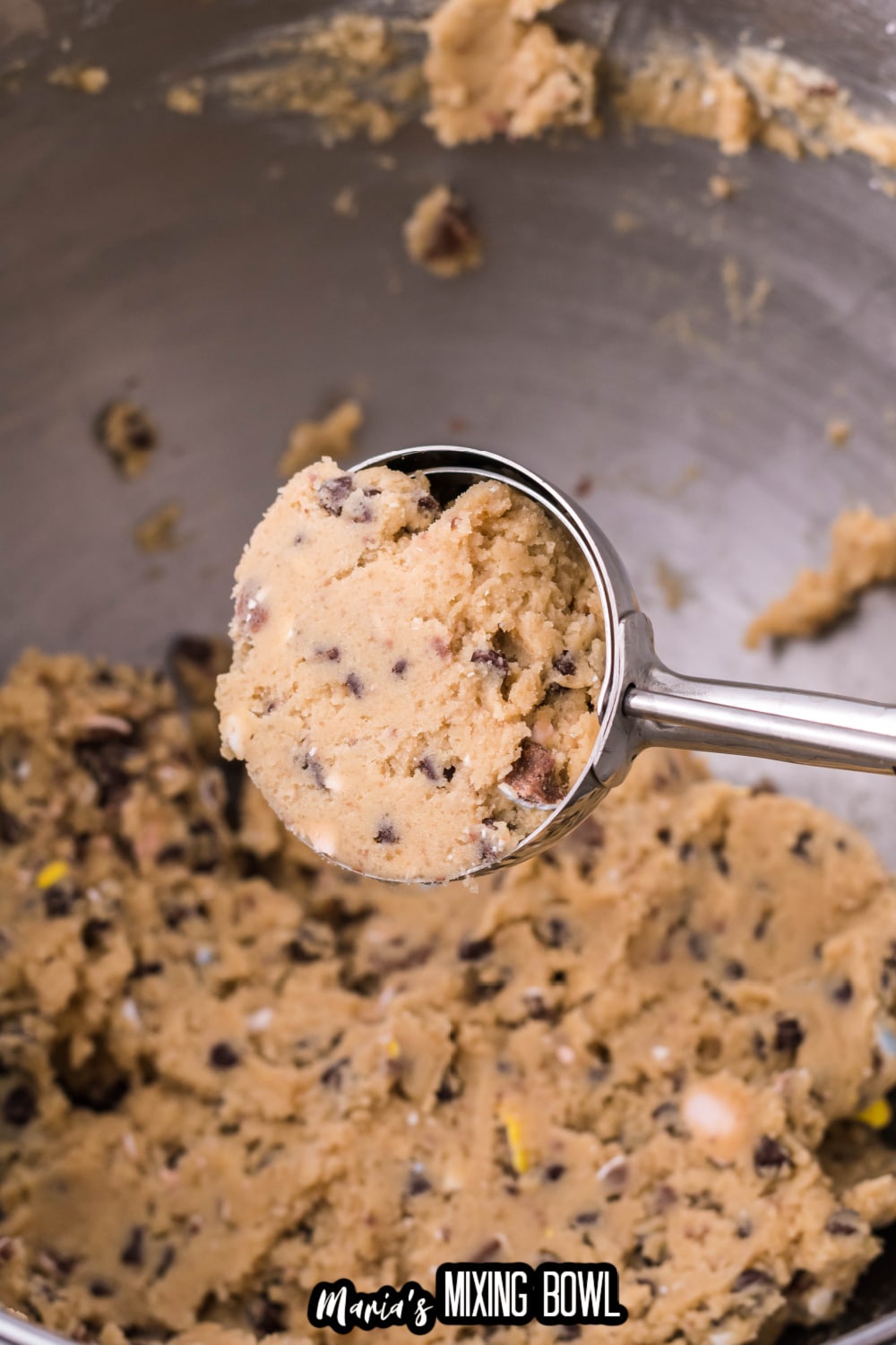 cookie dough in a cookie scoop held above a mixing bowl full of dough